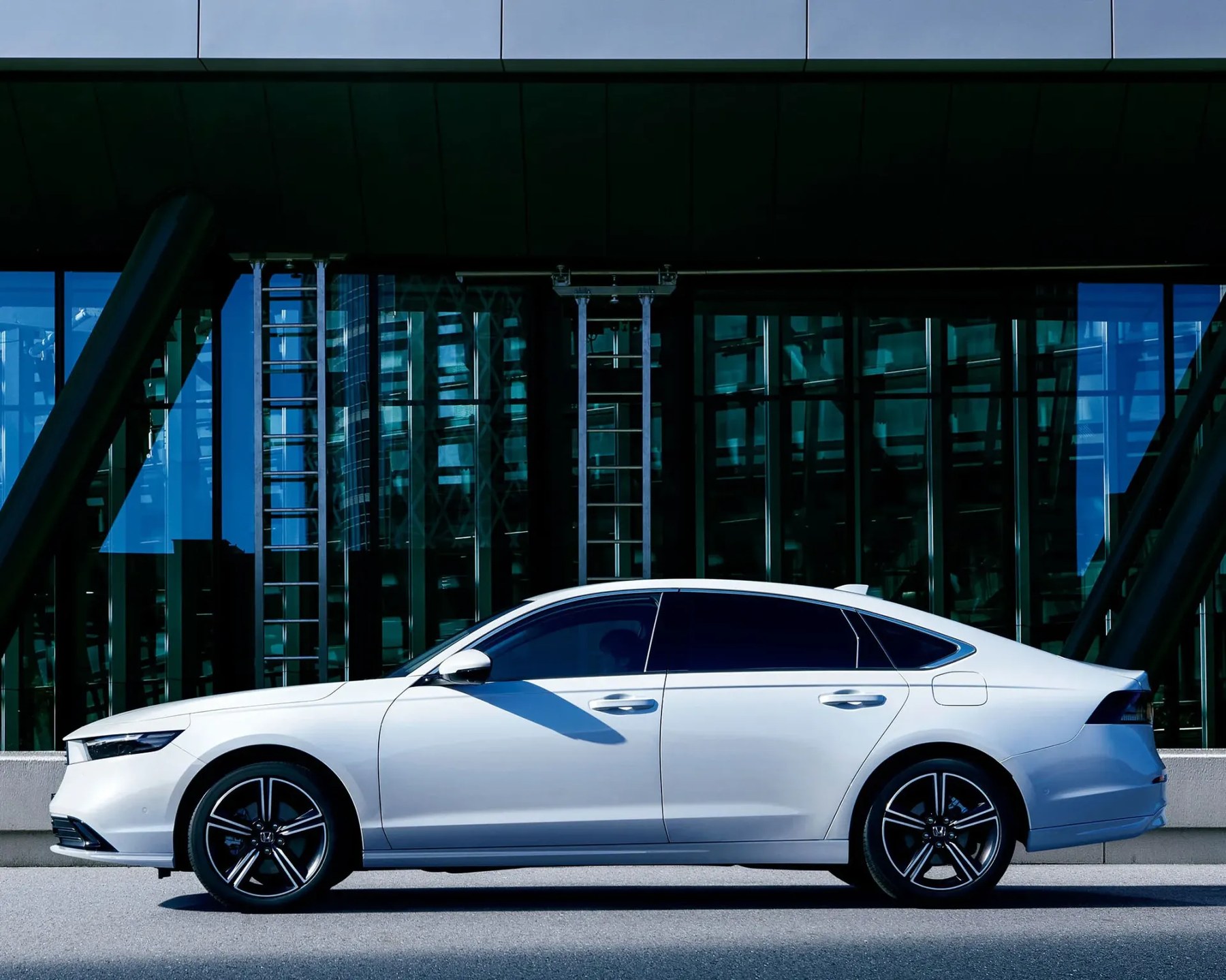 White Honda sedan parked in front of a modern glass building with black structural beams.