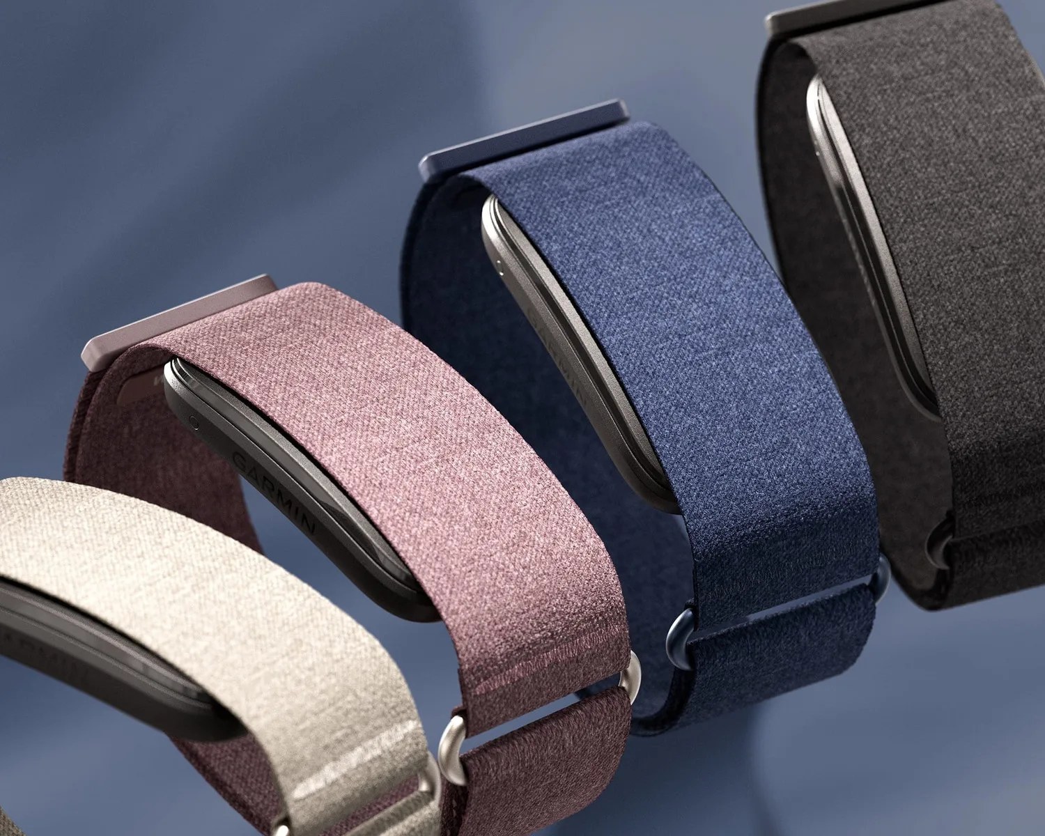 Four smartwatches with fabric bands in beige, mauve, blue, and black on a blue surface.