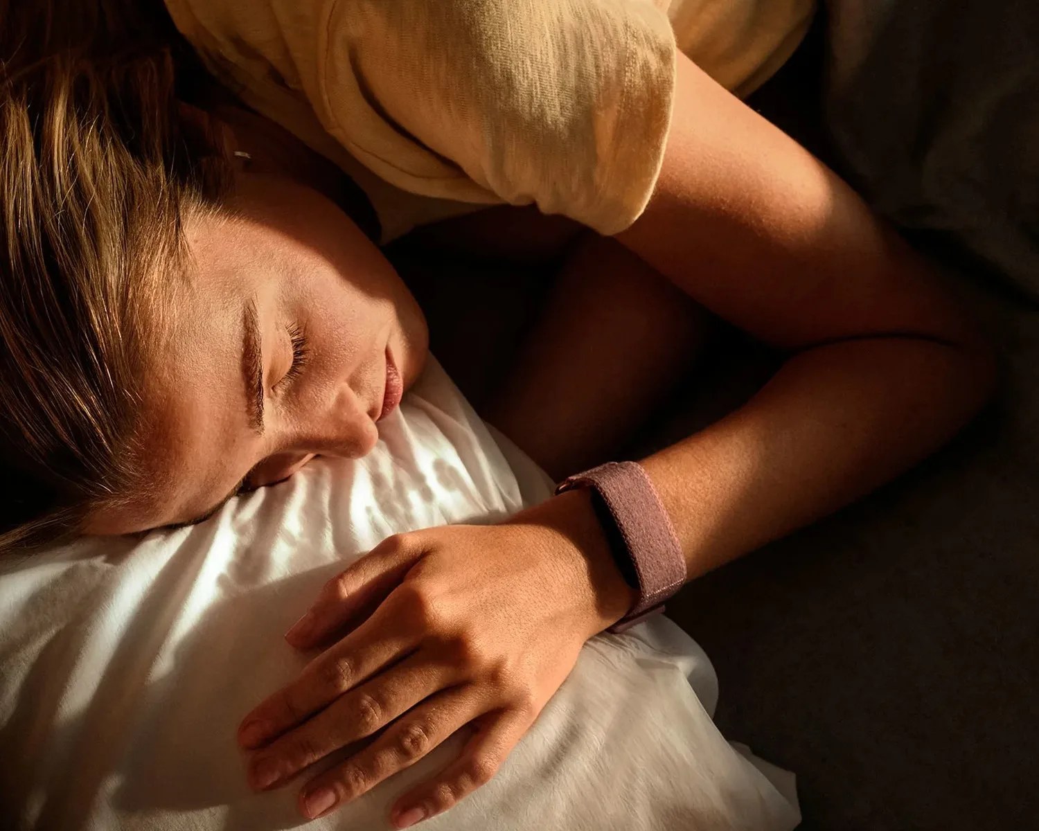 Person sleeping on a white pillow wearing a beige shirt and a brown fabric wristband.